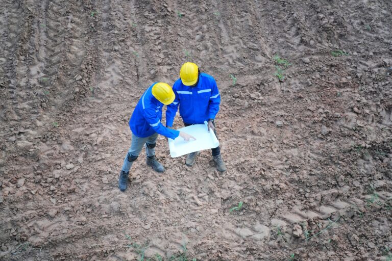 Top view two engineers discussing over blueprint on land at wind turbine site.